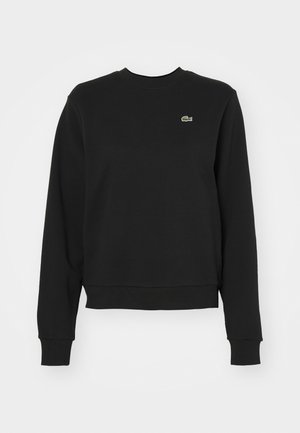 Črna majica s kapuco iz mešanice bombaža, z rebrastim vratnim izrezom in manšetami. Ima majhen zelen logotip Lacoste na prsih. Klasičen kroj.