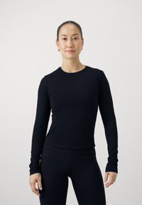 Maglietta nera a maniche lunghe in tessuto liscio, con scollatura rotonda e design aderente. Abbinata a leggings neri coordinati.