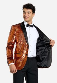 Blazer naranja con lentejuelas y solapas negras, cierre de botón único y bolsillo interior, llevado sobre una camisa blanca y corbata negra.