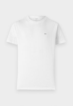 Camiseta de algodón blanca con cuello redondo clásico, mangas cortas y un pequeño logo gris de GAP en el lado izquierdo del pecho. Diseño simple y sin adornos.