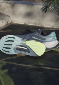 Hardloopschoenen voor heren met een grijze bovenkant, blauwe accenten en een opvallende mintgroene buitenzool. Voorzien van texturen en een onderscheidend profiel.