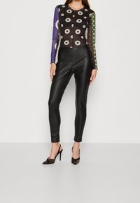 Leggings in pelle nera abbinati a una maglietta a maniche lunghe in rete con motivo, caratterizzata da maniche colorate e design floreali. Scarpe nere con tacco alto.