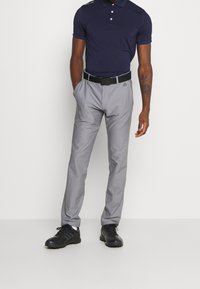 Marinblå pikétröja med treknapplik, grå golfbyxor med en slät textur och svarta sportskor med ett mönstrat sål. Svart bälte ingår.