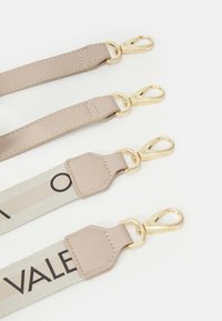 Due cinture in tessuto beige e crema, con accessori dorati. Una delle cinture presenta un logo e un motivo a contrasto; texture liscia su tutta la superficie.