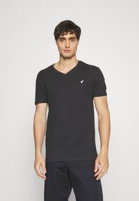 Black cotton t-shirt with a V-neck and short sleeves, featuring a small white logo on the left chest. Soft texture, casual fit.