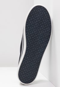 Schwarze Sneaker-Sohle mit einem strukturierten Gummi-Profil und weißer Zwischensohle. Das Design umfasst strukturierte Rillen für Grip und Stabilität.