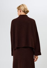 Ruskea ylisuuri neulepaita, jossa on lyhyt helma ja pitkät hihat. Pehmeä rakenne rentoon istuvuuteen, jossa on puolikorkea kaulus ja käännetyt hihansuut.