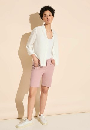 Chemise blanche légère à boutons, shorts rose ajustés et baskets blanches. Texture douce, design décontracté et shorts jusqu'aux genoux avec poches.