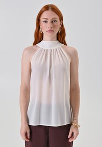 Blusa senza maniche di colore crema con colletto alto, caratterizzata da tessuto arricciato sul davanti e una silhouette fluida. Texture liscia e leggera.