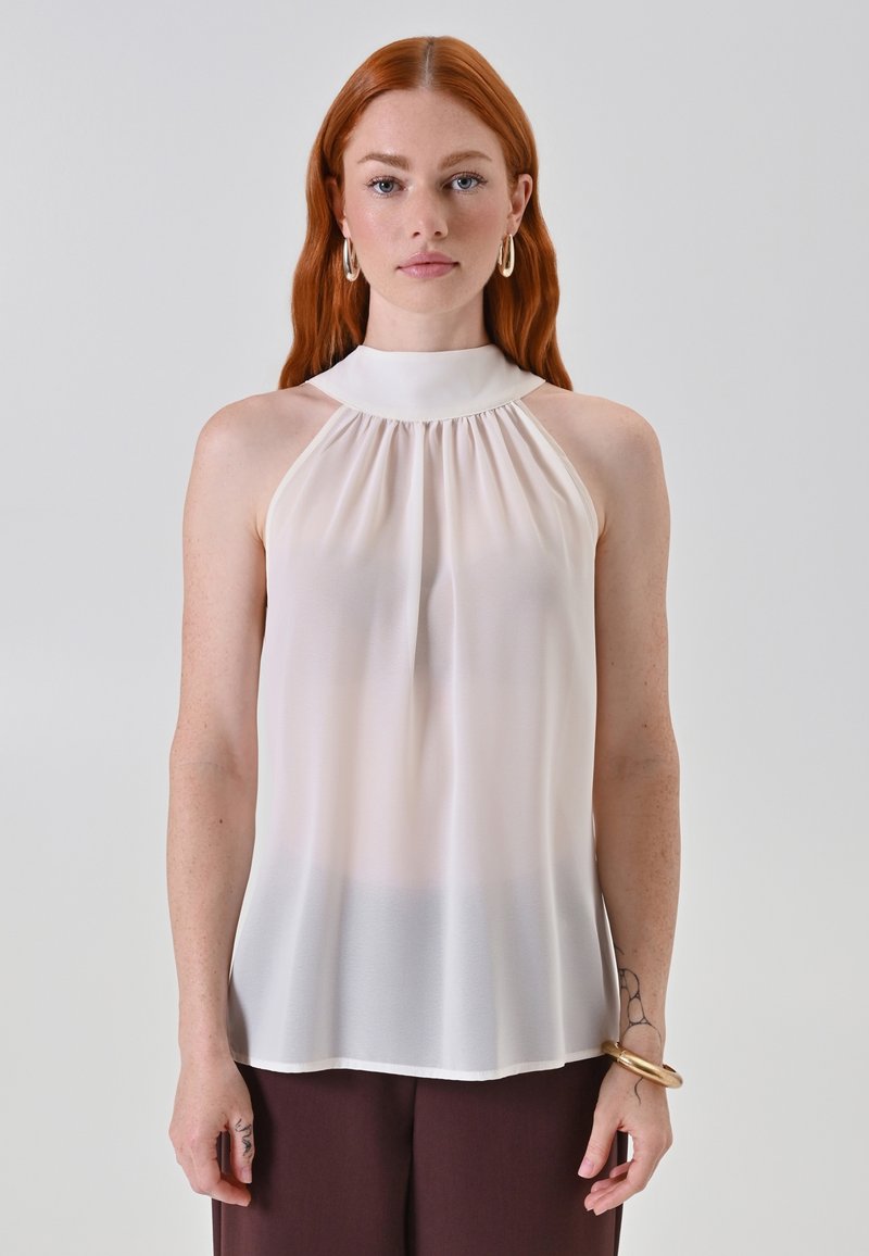 Blusa senza maniche di colore crema con colletto alto, caratterizzata da tessuto arricciato sul davanti e una silhouette fluida. Texture liscia e leggera.