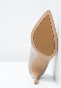 Chaussure à talon haut beige avec un bout pointu, dessus en cuir lisse et talon aiguille élancé. Semelle en caoutchouc avec texture subtile et logo.