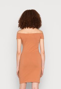 Vestido justo, com decote ombro a ombro, em tecido suave e elástico. Apresenta uma cor terracota sólida e um comprimento até a metade da coxa.