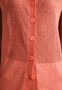 Cardigan leggero in maglia corallo con design a rete, dotato di sei bottoni rotondi e polsini a costine. Si distingue per il suo pattern testurizzato.