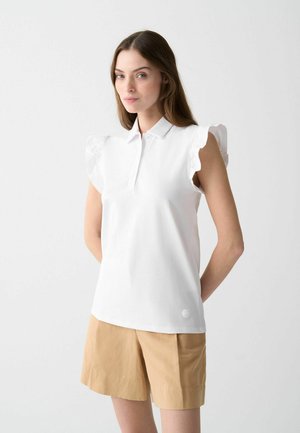 Witte poloshirt met gerimpelde korte mouwen, zachte stof en een subtiele logoaccent near de zoom, gecombineerd met beige shorts.