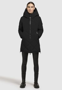 Mustvalge voodriga puffjakker, millel on kõrge kaelus ja suur kapuuts. Varustatud ees oleva tõmbluku ja küljetaskutega. Kantud mustade retuuside ja saapatega.