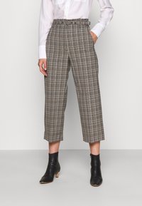 Bruna och grå rutiga byxor med hög midja som har bälte, vida avklippta ben och sidofickor, kombinerat med svarta ankelstövlar.