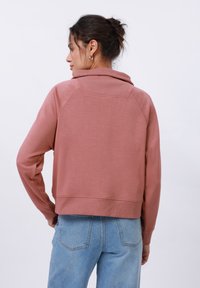 Rosa cropped sweatshirt med høy krage, ribbestrikkede kanter og raglanermer, parret med lyseblå høy midje jeans.