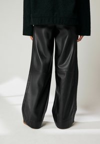 Pantalons en cuir noir taille haute, à jambe large et au toucher lisse, présentant des coutures sur le devant et une coupe ample pour le confort.