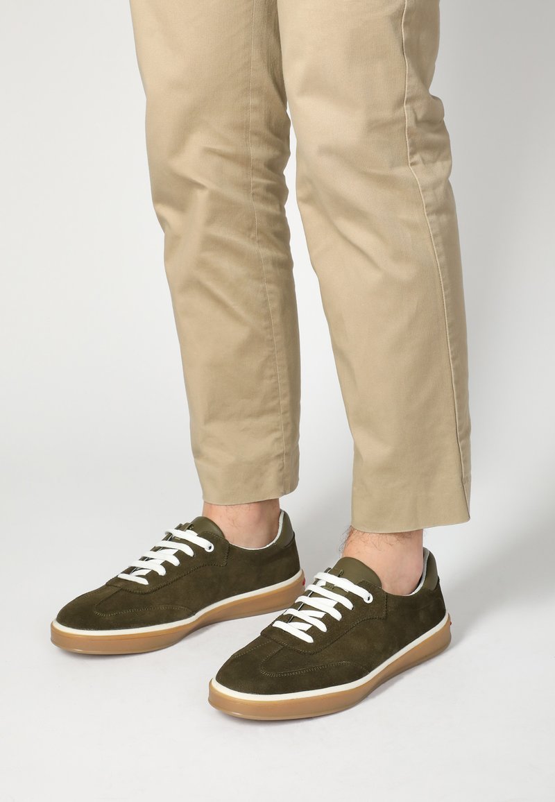 Grüne Wildledersneaker mit weißen Schnürsenkeln, einer strukturierten Oberseite und einer hellbraunen Gummisohle, kombiniert mit hellbeigen Hosen.