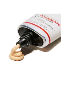 Tubka z ciemnym aplikatorem, zawierająca beżowy produkt podkładowy o gładkiej teksturze, oznaczona napisem „Photo Finish Illuminate Glow Primer.”