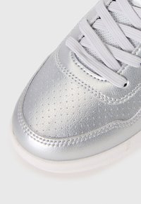 Baskets en cuir argenté avec texture perforée, lacets blancs et semelle en caoutchouc. Design courbé à la pointe avec des accents cousus.