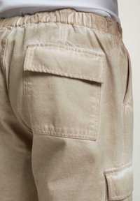 Vaaleat beige cargo-shortsit, joissa on joustava vyötärö, ommeltu sivutasku ja pehmeä kangas. Muotoilussa on yksi takatasku.