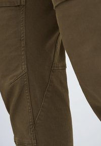 Olive green cargo pants with a textured fabric, featuring side pockets and visible seams in a tapered design.