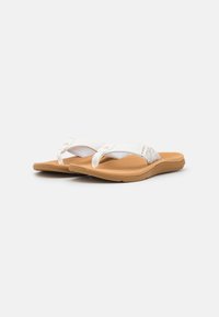 Hvite flip-flops med en teksturert brun såle, med stoffstropper og et bladmønster som aksent på den øverste remmen.