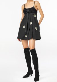 Černé bezramínkové šaty s plisovanou sukní, zdobené květinovou výšivkou a smockovaným živůtkem. V páru se svršky nad kolena z černé surové kůže.