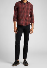 Červeno-černá kostičkovaná flanelová košile s knoflíkovými manžetami, spárovaná s černými slim-fit kalhotami a černými šněrovacími botami se žlutými akcenty.