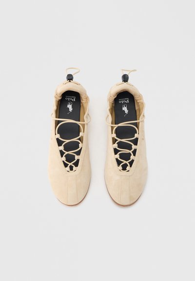 Μπεζ παπούτσια από σουέτ με στρογγυλεμένη μύτη και σχέδιο με κορδόνια που διαθέτει κυκλικές εγκοπές. Μαύρη εσωτερική σόλα με λογότυπο. Ομαλή υφή και μινιμαλιστικό σχήμα.