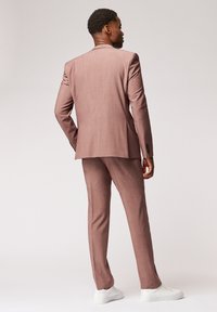 Jasnoróżowy garnitur o teksturowanym wykończeniu, jednorzędowa marynarka, slim fit spodnie i białe trampki. Widok z tyłu.
