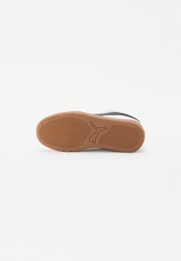 Sneaker bianco con accenti neri e suola in gomma testurizzata. Presenta un motivo ondulato sulla suola e un logo sul tallone.
