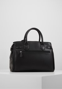 Sac à main en cuir noir avec double poignée, une poche zippée à l'avant et une forme rectangulaire structurée sur un socle blanc.