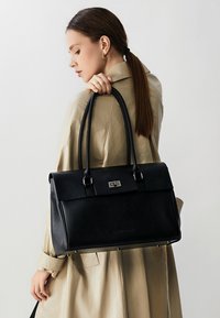Borsa tote in pelle nera con design strutturato, hardware argentato, doppie maniglie e superficie liscia e texture.
