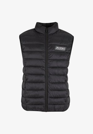 Black padded vest with a high collar, vertical quilted design, zip front, and a logo patch on the left side. Lightweight and sleeveless.