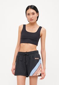 Top corto negro combinado con pantalones cortos grises que presentan un patrón diagonal en azul y melocotón, cinturilla con cordón y detalle de logo.