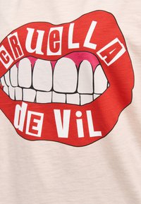 Světle barevná košile s grafikou červených rtů s bílými zuby, ozdobená nápisem "CRUELLA de VIL" ve stylizovaném písmu.