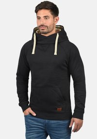 Black hoodie with a funnel neck, beige drawstrings, front pocket, and a small brown label. Features a soft texture and fitted design.