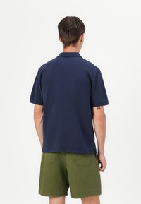 Marineblå kortermet poloskjorte laget av bomull med klassisk krage. Kombinert med olivengrønne shorts som har to baklommer.