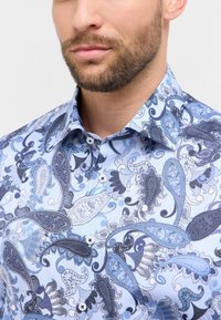 Lichtblauw shirt met een paisleypatroon in donkerblauw en grijs. Button-down kraag, witte knopen en een soepele stoftextuur.