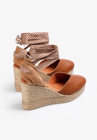 Brune læder espadrille wedges med vævede tekstilremme, rund tå og jutebeklædt kilehæl. Remmene har et ternet mønster.