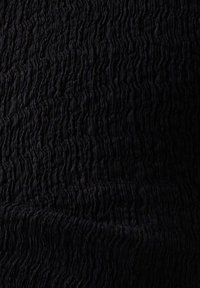 Tissu noir texturé avec une surface froissée, présentant des crêtes irrégulières et un motif ondulé, créant profondeur et dimension.