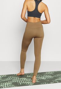 Leggings marroni a vita alta con una texture liscia, abbinati a un reggiseno sportivo racerback grigio scuro, su un tappetino da esercizio a motivi.