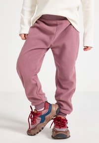Fleece-Jogginghosen in sanftem Rosa mit elastischem Bund, lockerer Passform und gerippten Bündchen. Kombiniert mit mehrfarbigen Sportschuhen mit strukturierten Sohlen.