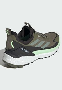 Zapato de senderismo verde oliva con acentos negros, parte superior de malla texturizada, suela verde claro y un destacado logo "TERREX" en el talón.