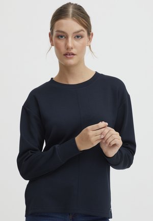 Mørkeblå hettegenser med rund hals, lange raglanermer og strukturert stoff. Har sømdetaljer langs fronten.