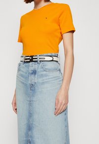 Oranžové bavlněné tričko s kulatým výstřihem a krátkým rukávem, spárované se světle modrou džínovou sukní, která má černobílý pásek.