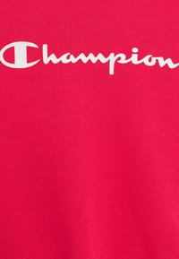 Červené bavlněné tričko s velkým bílým logem "Champion" umístěným na středu hrudi, hladká textura a standardní design s kulatým výstřihem.