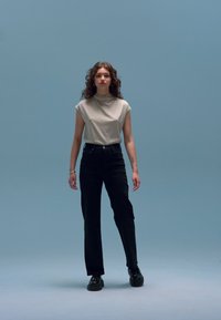 Helehall, varrukateta kaelusega top koos kõrge vöökohaga mustade pükste ja mustade kingadega. Lihtne disain sinisel taustal.